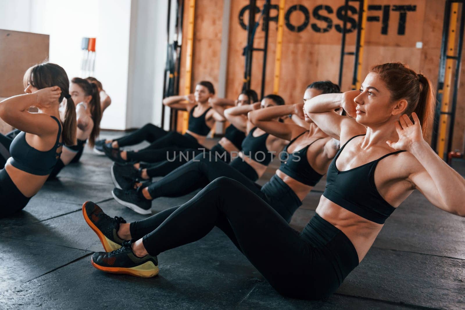 Doing abs. Group of young sportive people have crossfit day indoors in gym.