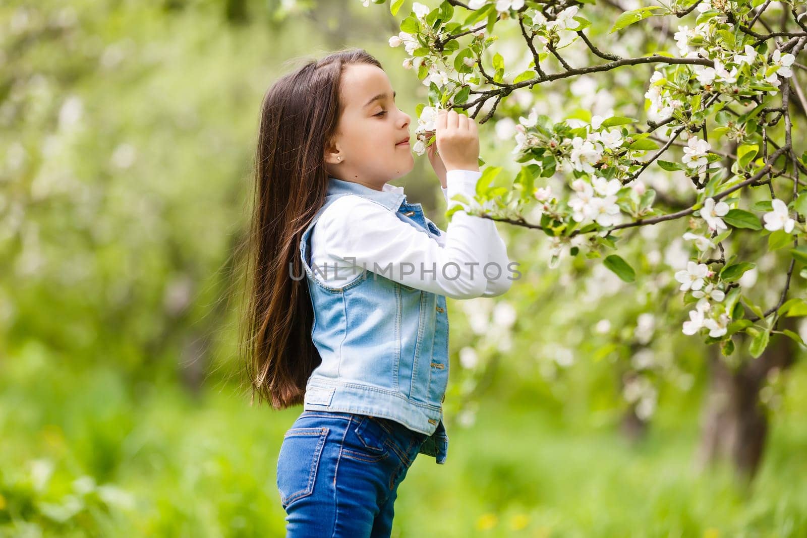 Portrait of cute and pretty little girl in spring blooming trees. Adorable little girl smiling in blooming garden on sunny day. Child and flowers. Childhood & natural tenderness. Children's day. by Andelov13