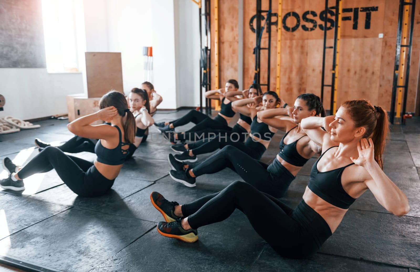 Doing abs. Group of young sportive people have crossfit day indoors in gym.