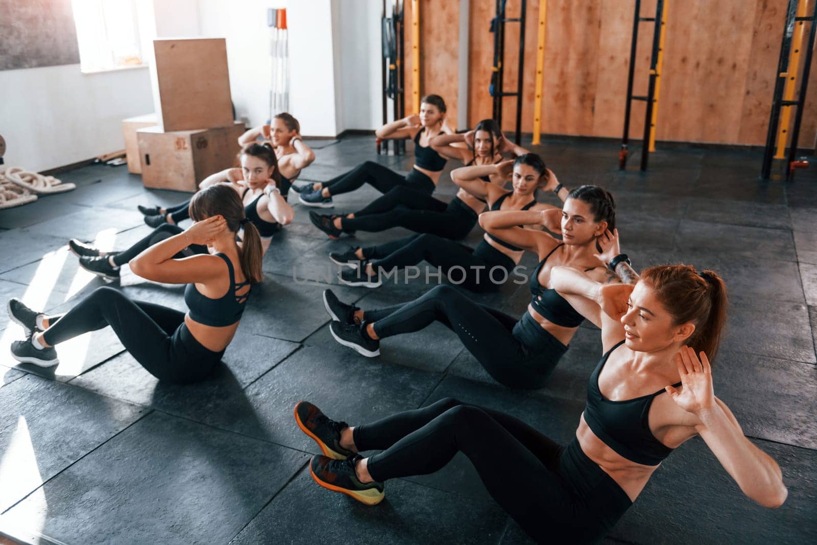 Doing abs. Group of young sportive people have crossfit day indoors in gym.