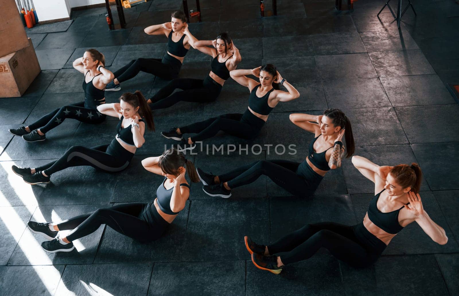 Doing abs. Group of young sportive people have crossfit day indoors in gym.
