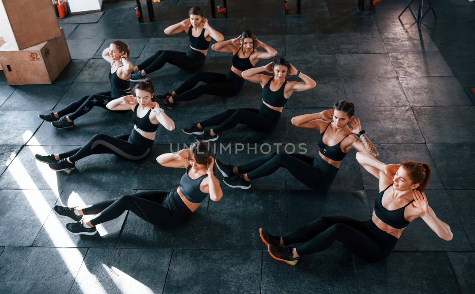 Doing abs. Group of young sportive people have crossfit day indoors in gym.