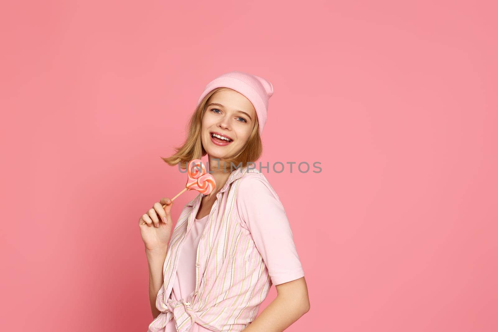 beautiful blonde woman holding candy on pink background.