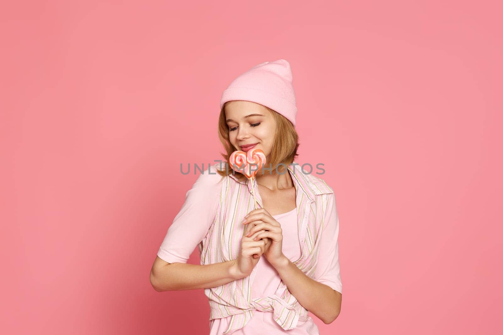 Lovely blonde woman holding colorful caramel candy on stick on pink background. copy space