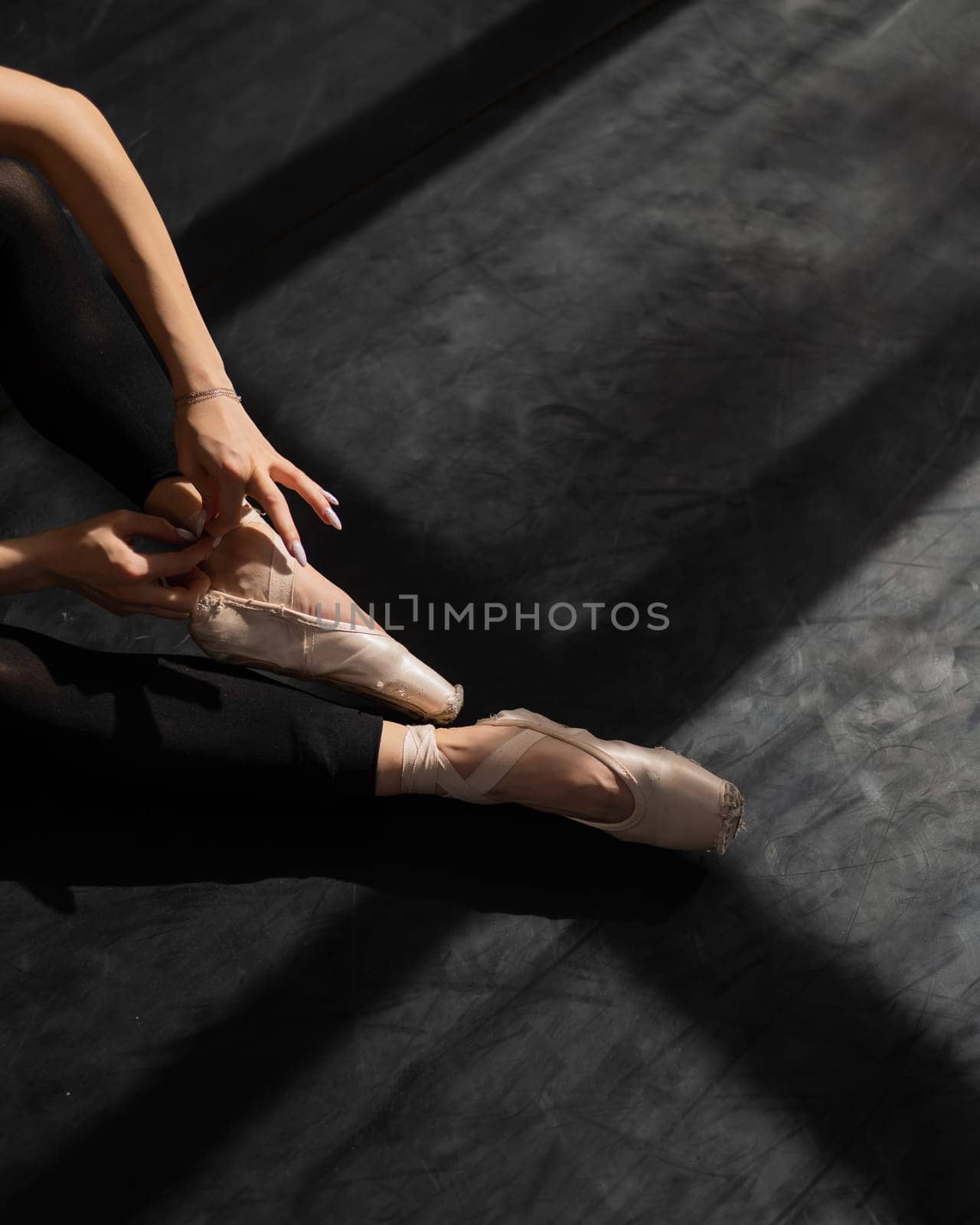 Faceless ballerina sits on the floor and puts on pointe shoes. Top view