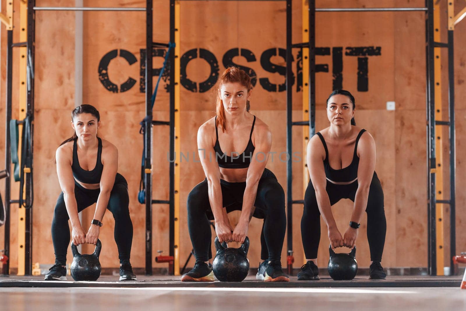Using barbells. Group of young sportive people have crossfit day indoors in gym.