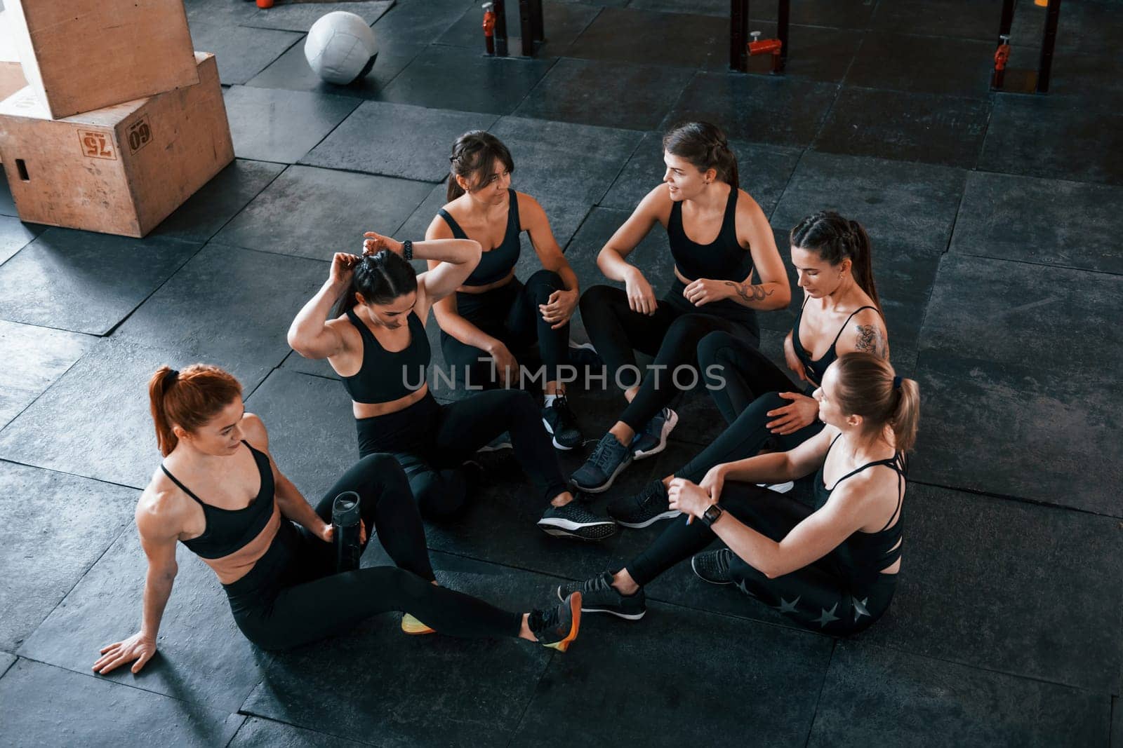 Sitting on floor. Group of young sportive people have crossfit day indoors in gym.