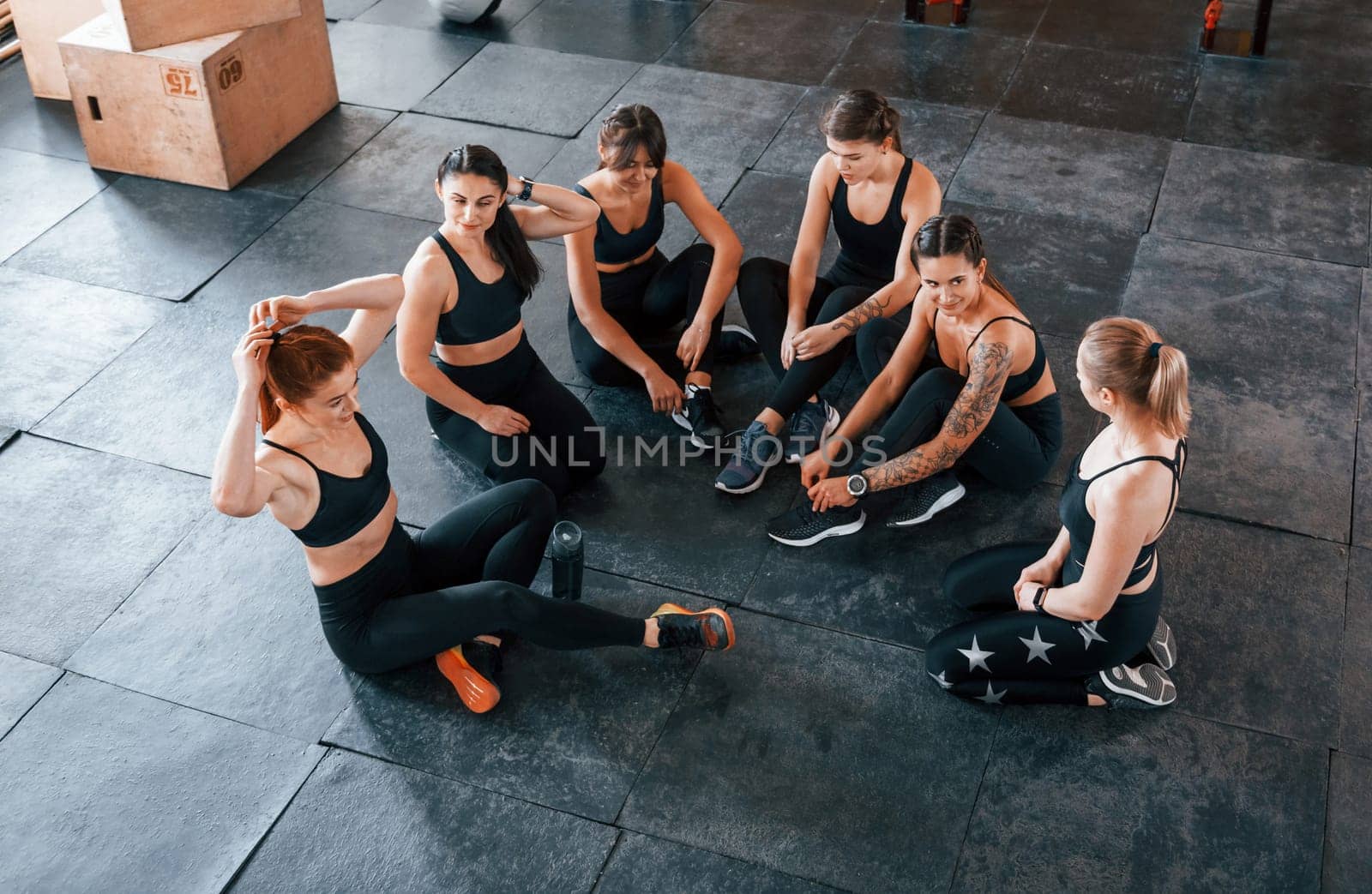 Sitting on floor. Group of young sportive people have crossfit day indoors in gym.