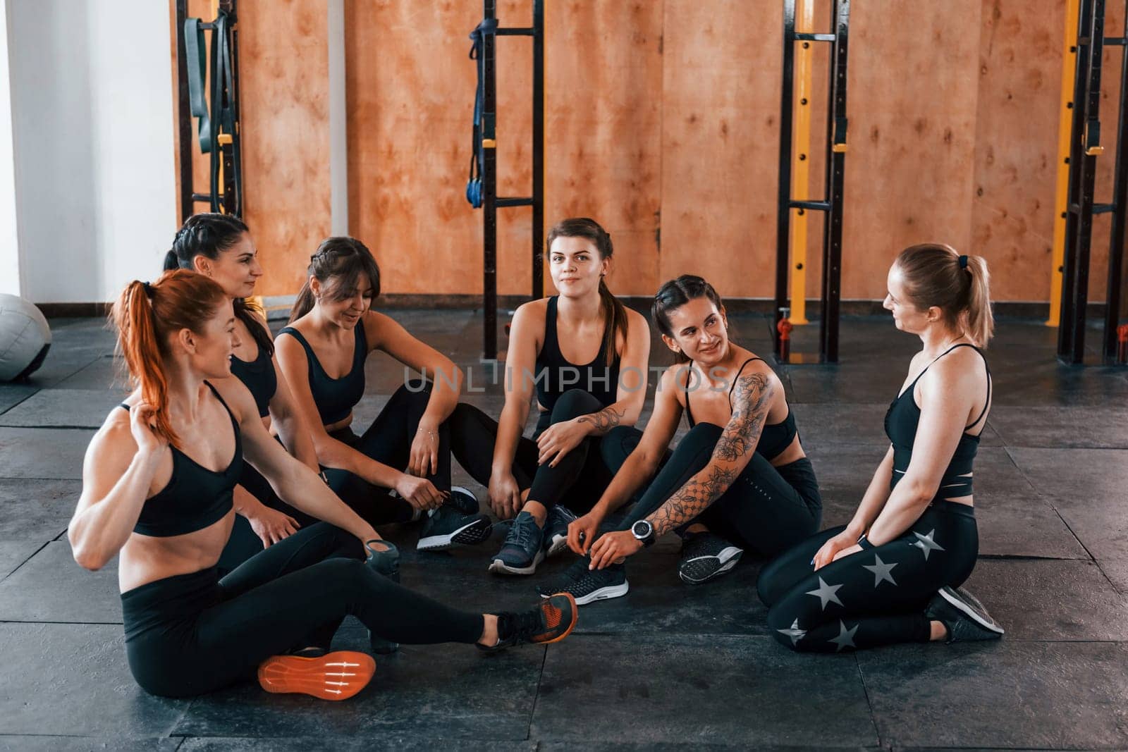 Sitting on floor. Group of young sportive people have crossfit day indoors in gym.