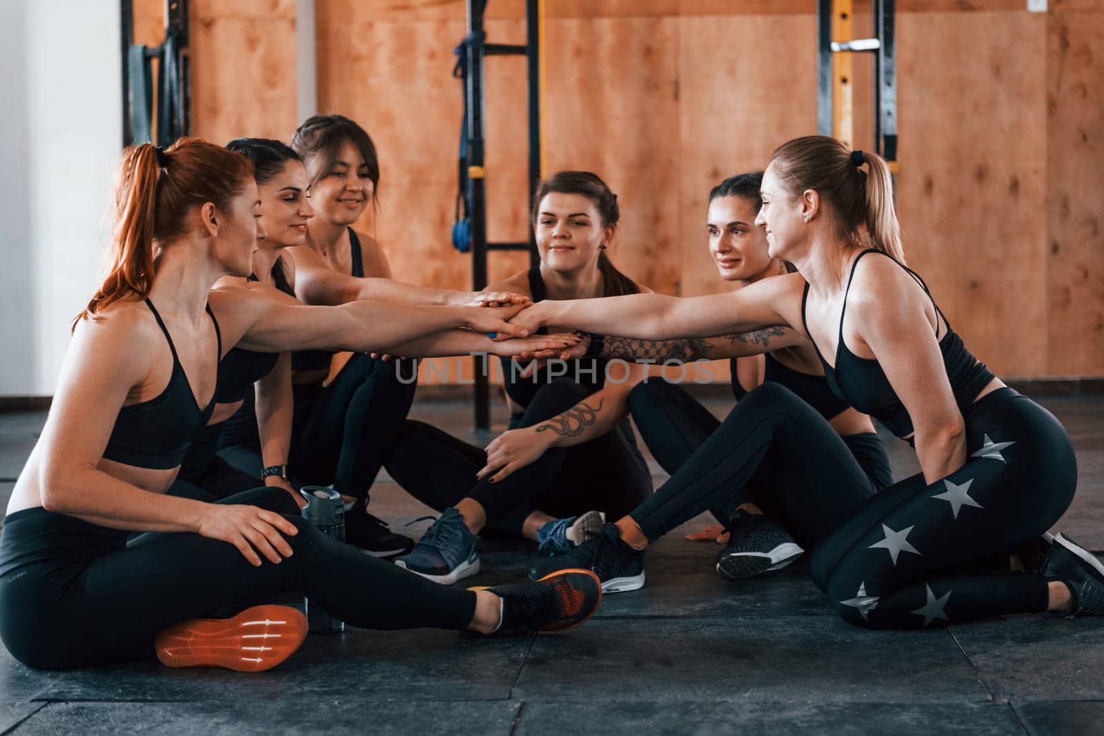 Sitting on floor. Group of young sportive people have crossfit day indoors in gym.