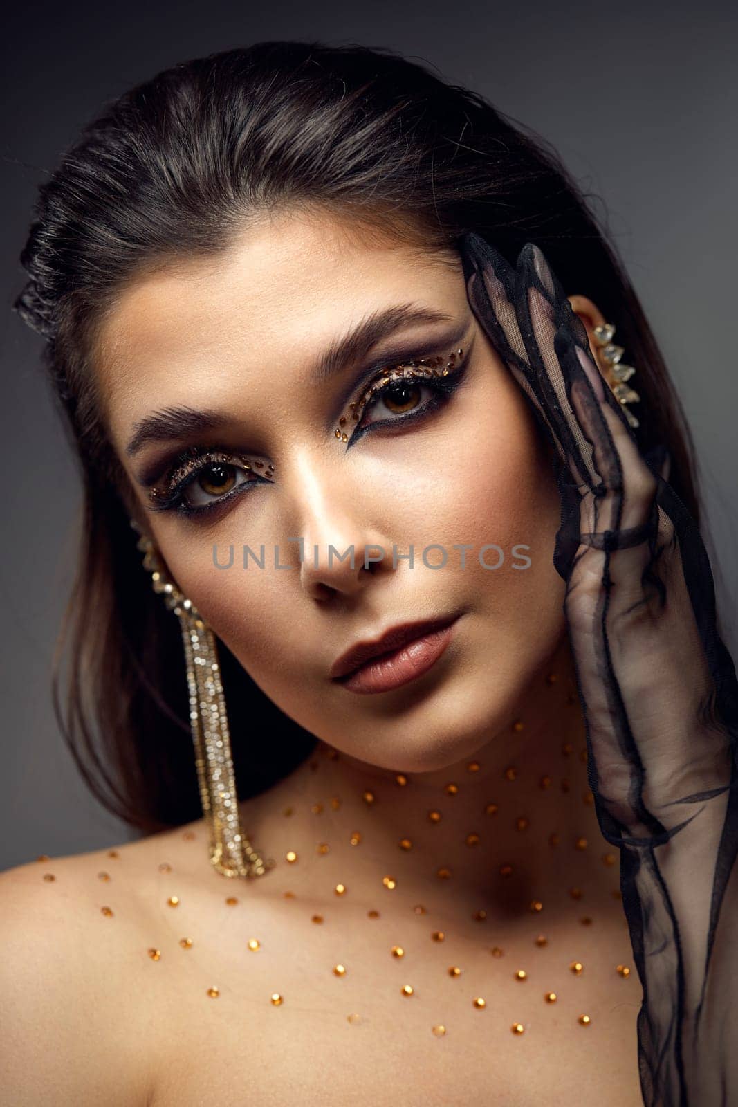 beauty fashionable model woman with creative eye makeup with arrows and rhinestones in long earring on gray background