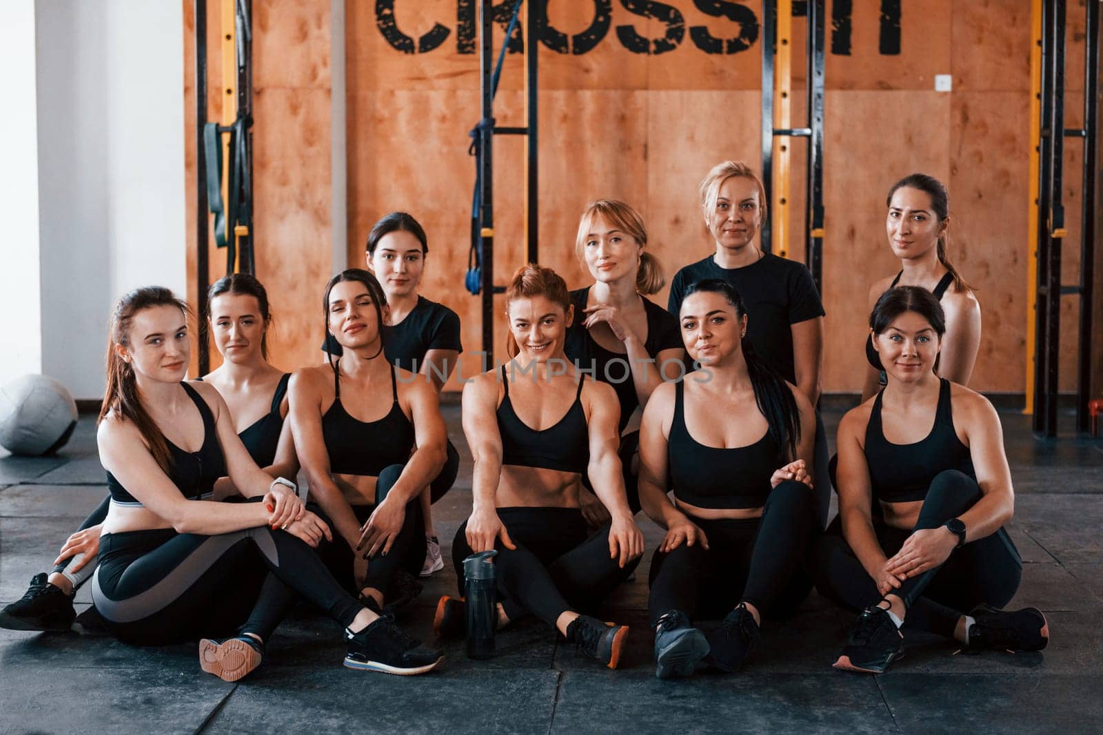 Sitting on floor. Group of young sportive people have crossfit day indoors in gym.