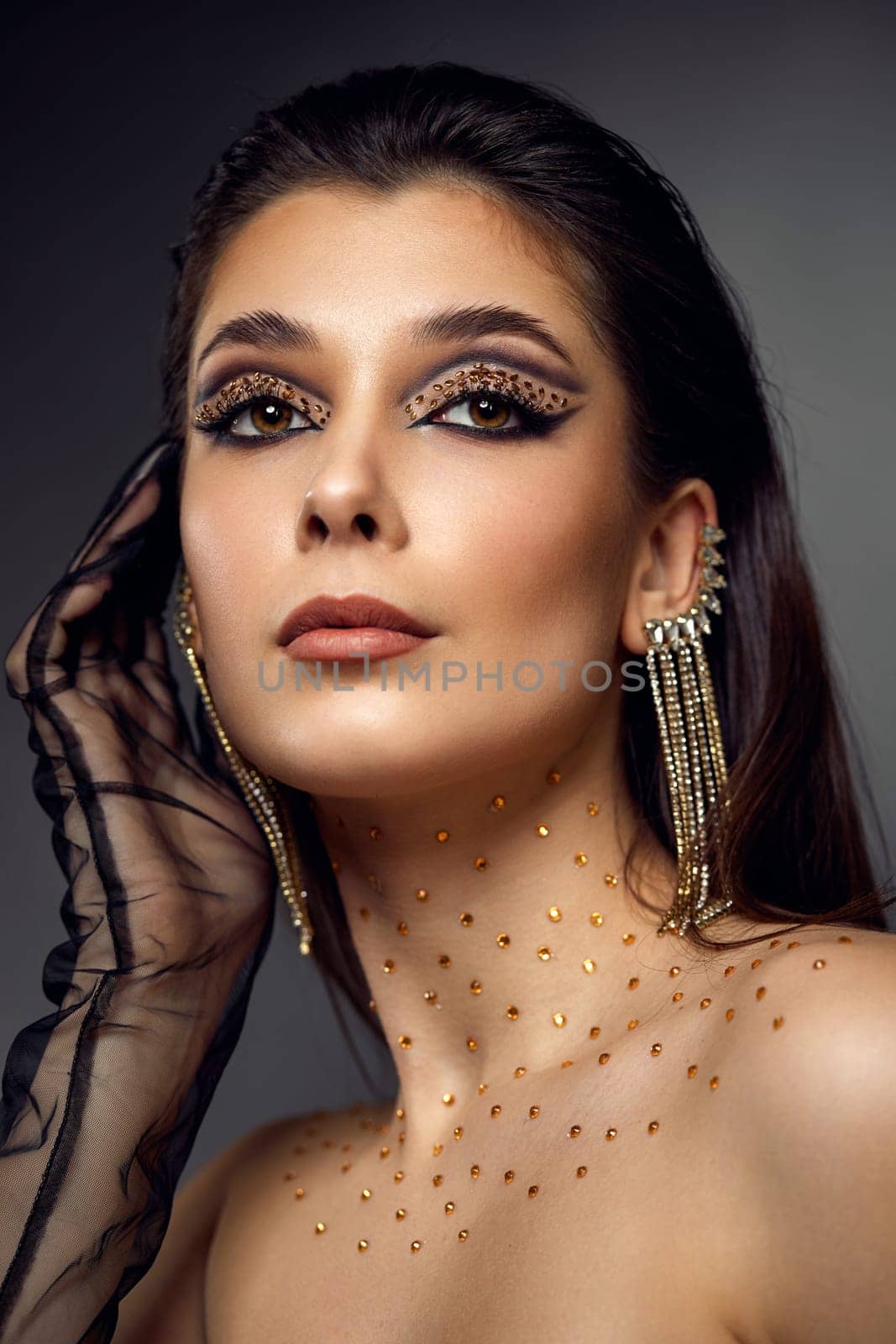beauty fashionable model woman with creative eye makeup with arrows and rhinestones in long earring on gray background