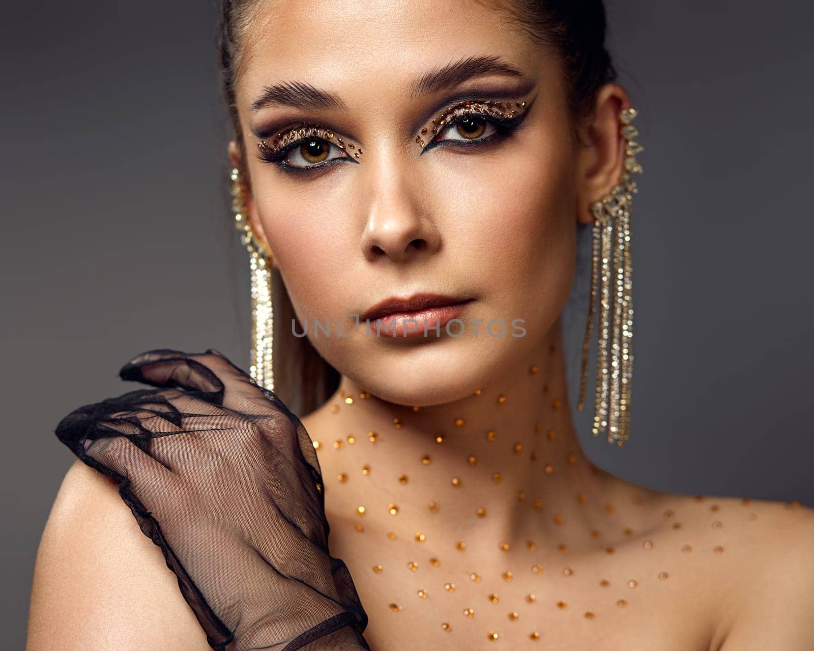 beauty fashionable model woman with creative eye makeup with arrows and rhinestones in long earring on gray background