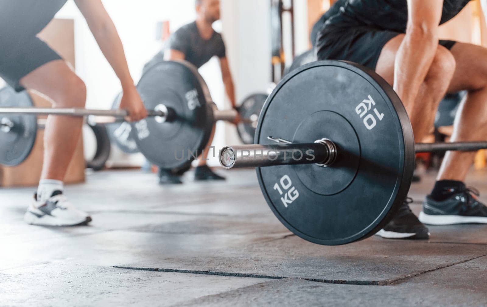 By using heavy weights. Group of young sportive people have crossfit day indoors in gym.
