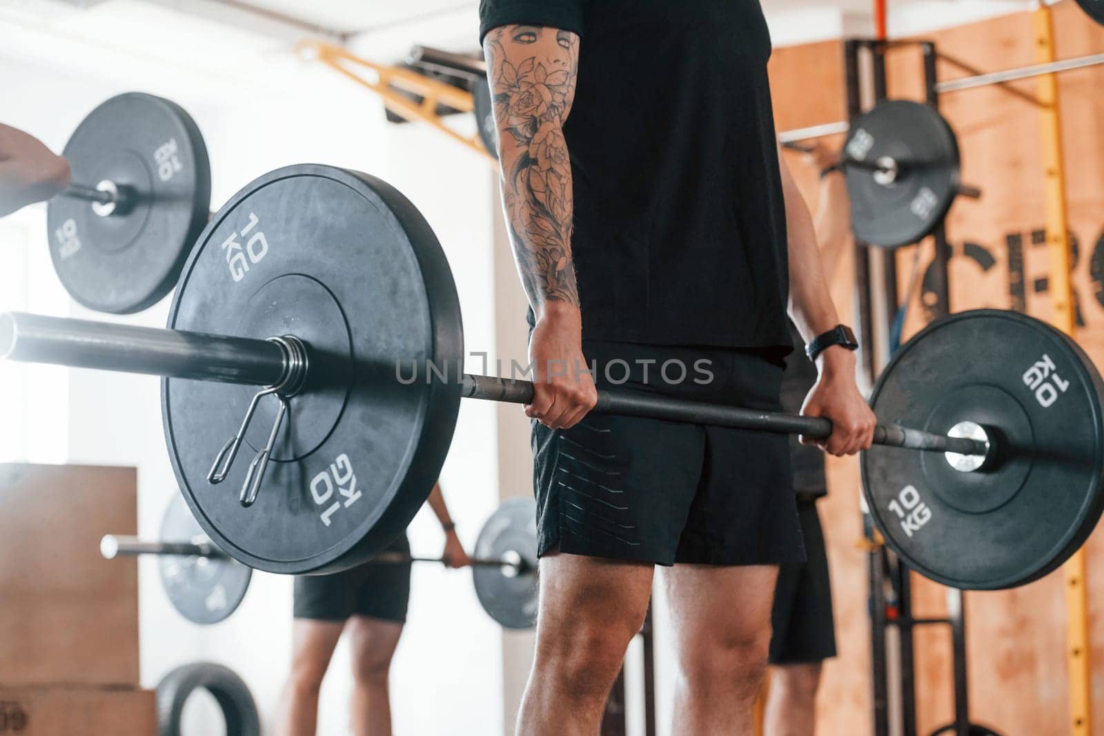 Lifting barbell. Group of young sportive people have crossfit day indoors in gym.