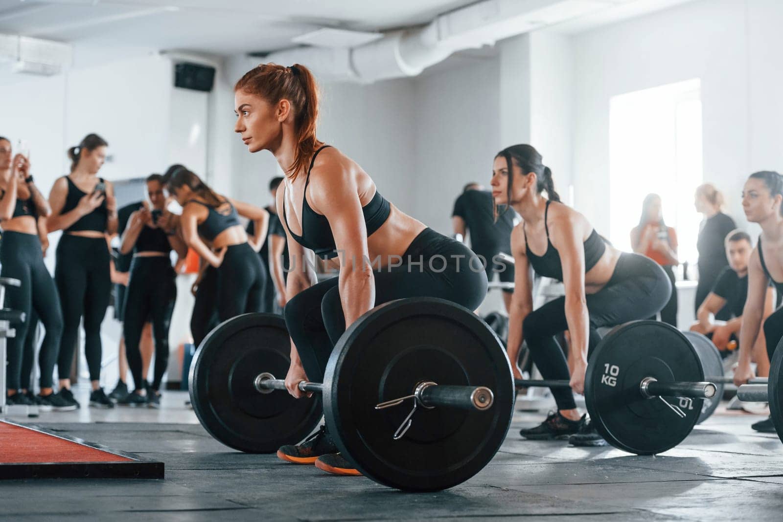 Lifting barbell. Group of young sportive people have crossfit day indoors in gym.