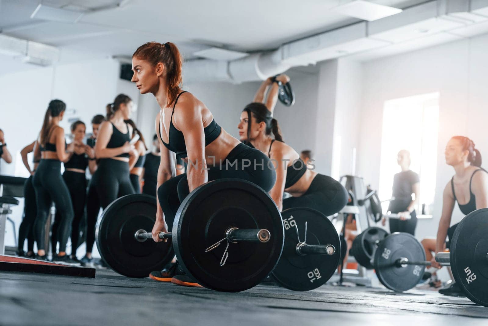 Lifting barbell. Group of young sportive people have crossfit day indoors in gym.