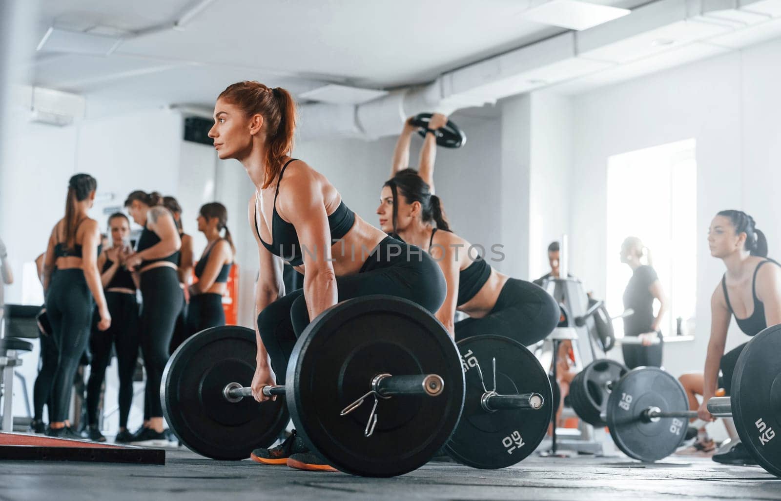 Lifting barbell. Group of young sportive people have crossfit day indoors in gym.