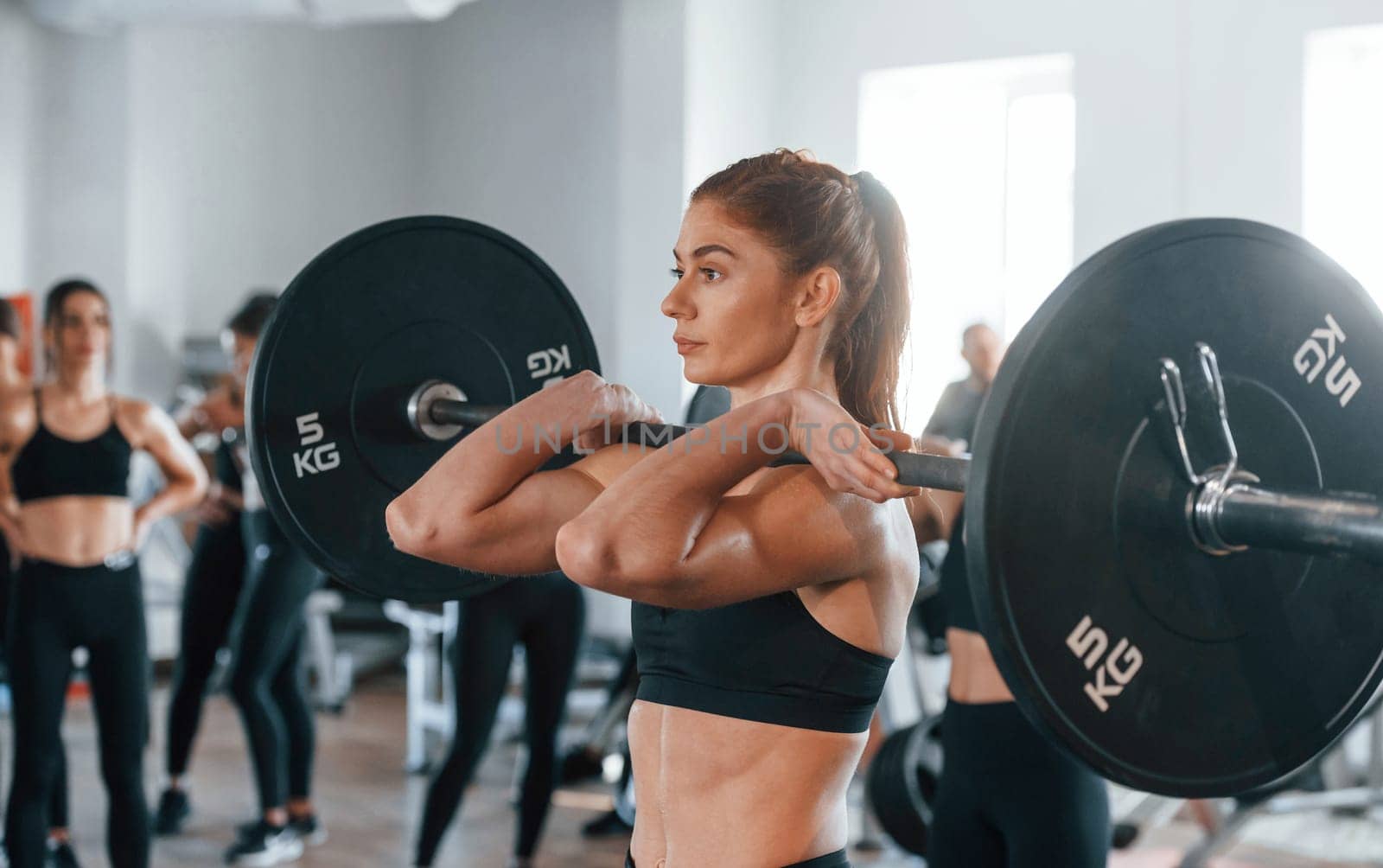 Lifting barbell. Group of young sportive people have crossfit day indoors in gym.
