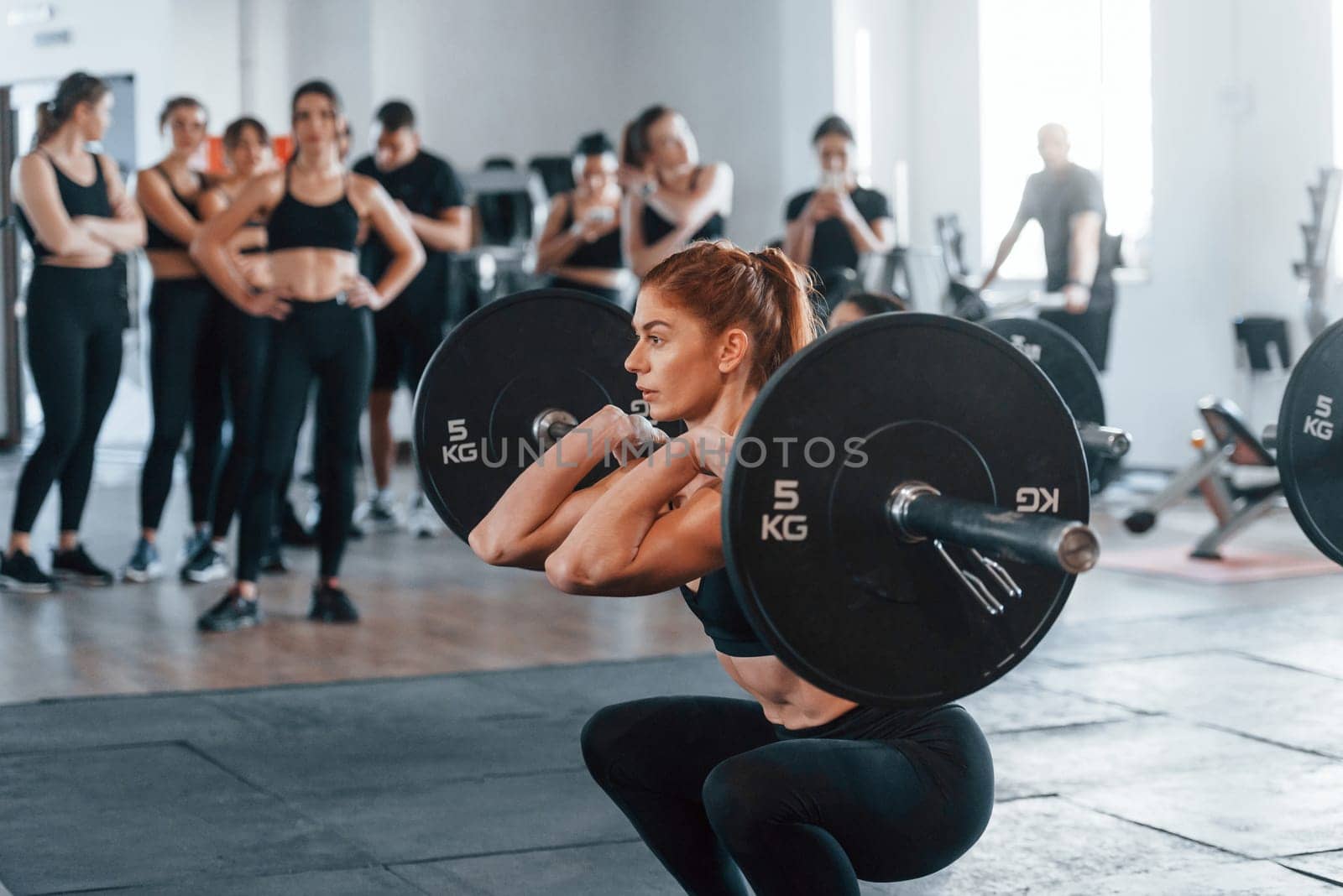 Lifting barbell. Group of young sportive people have crossfit day indoors in gym.