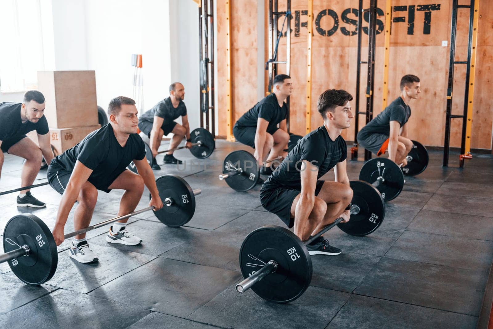Busy by doing exercises. Group of young sportive people have crossfit day indoors in gym.