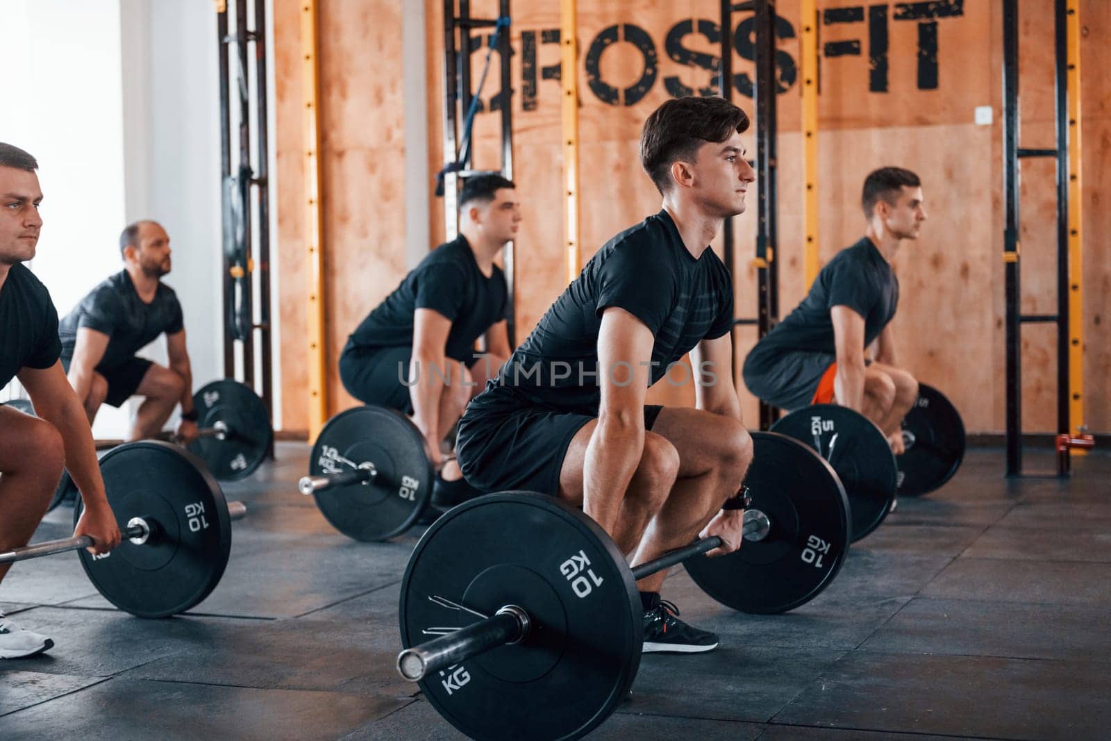 Busy by doing exercises. Group of young sportive people have crossfit day indoors in gym.