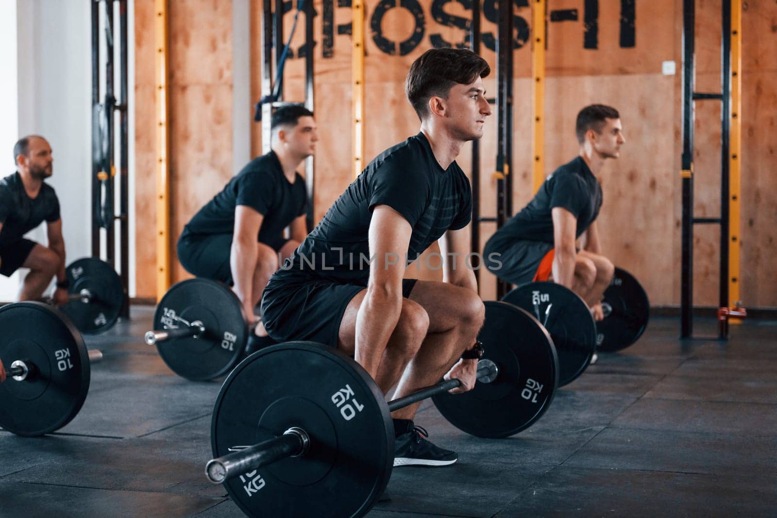 Busy by doing exercises. Group of young sportive people have crossfit day indoors in gym.