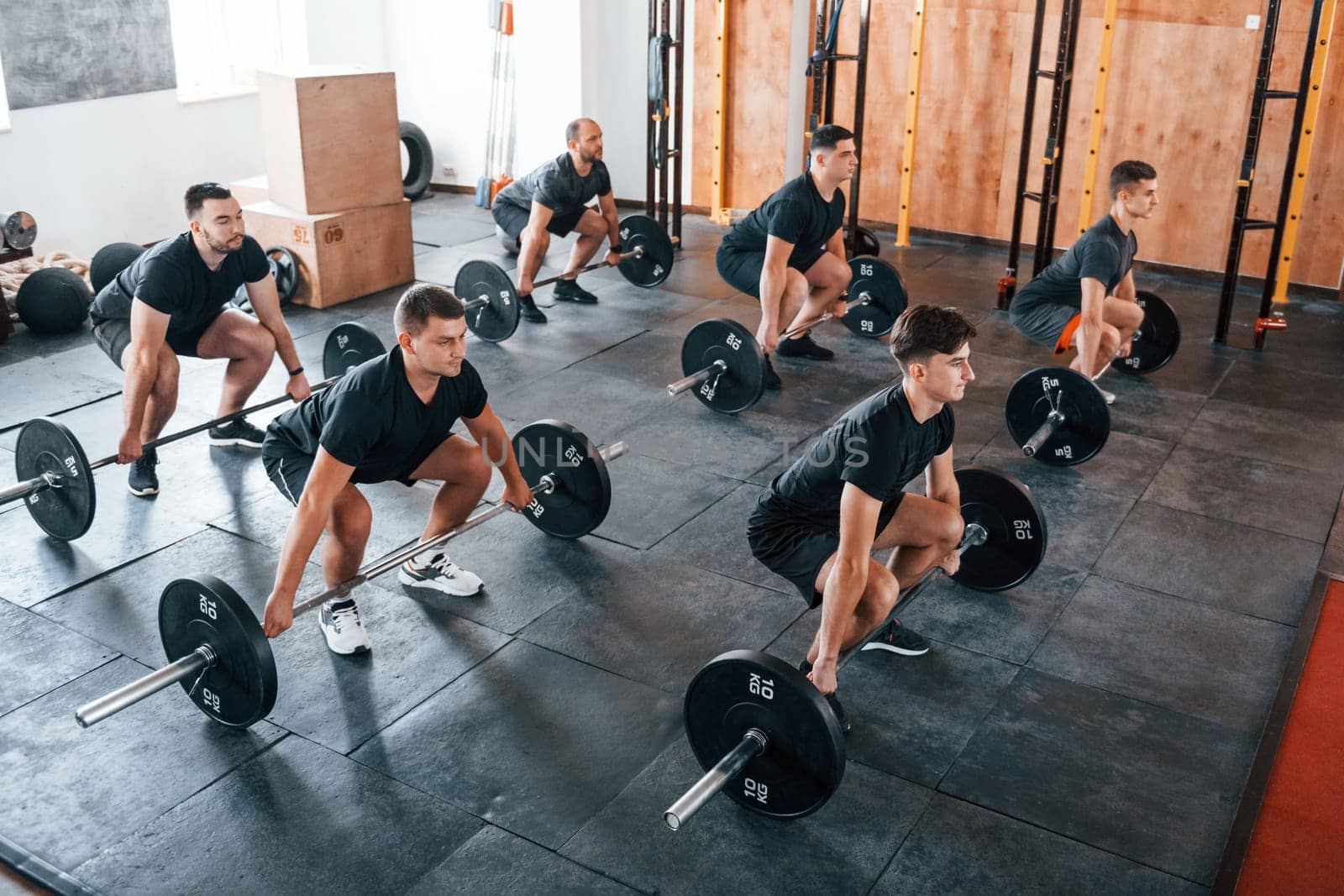 Busy by doing exercises. Group of young sportive people have crossfit day indoors in gym.