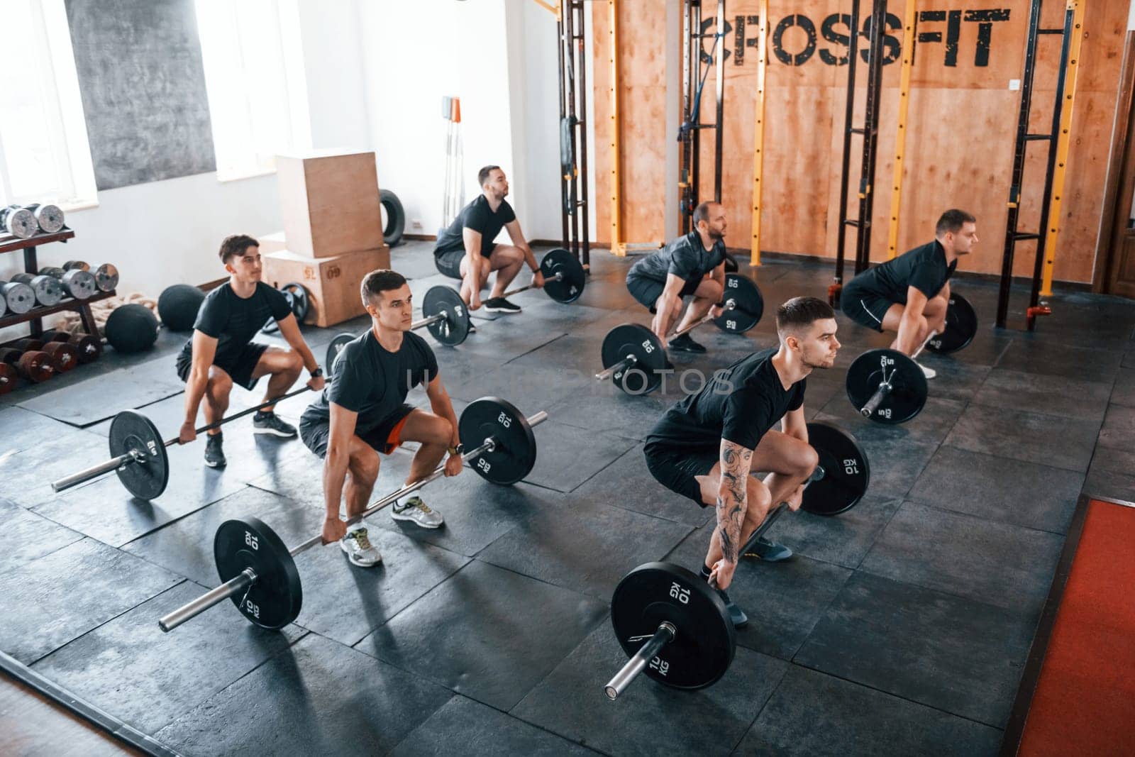 Busy by doing exercises. Group of young sportive people have crossfit day indoors in gym.