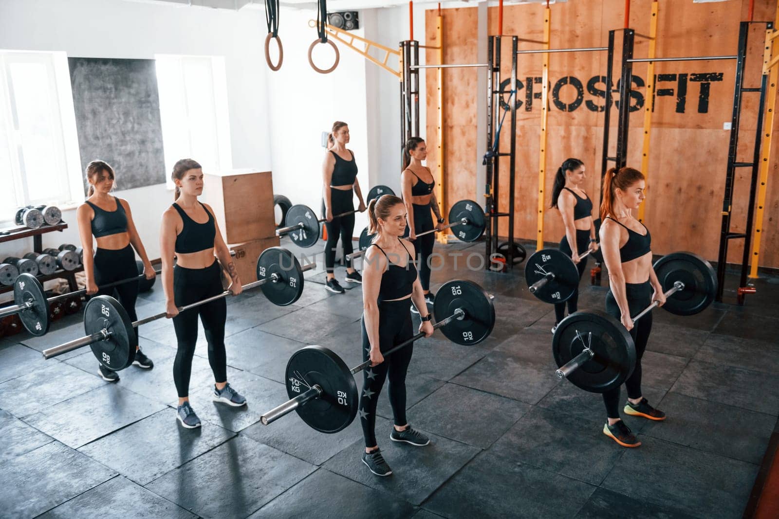 Together with barbells. Group of young sportive people have crossfit day indoors in gym.