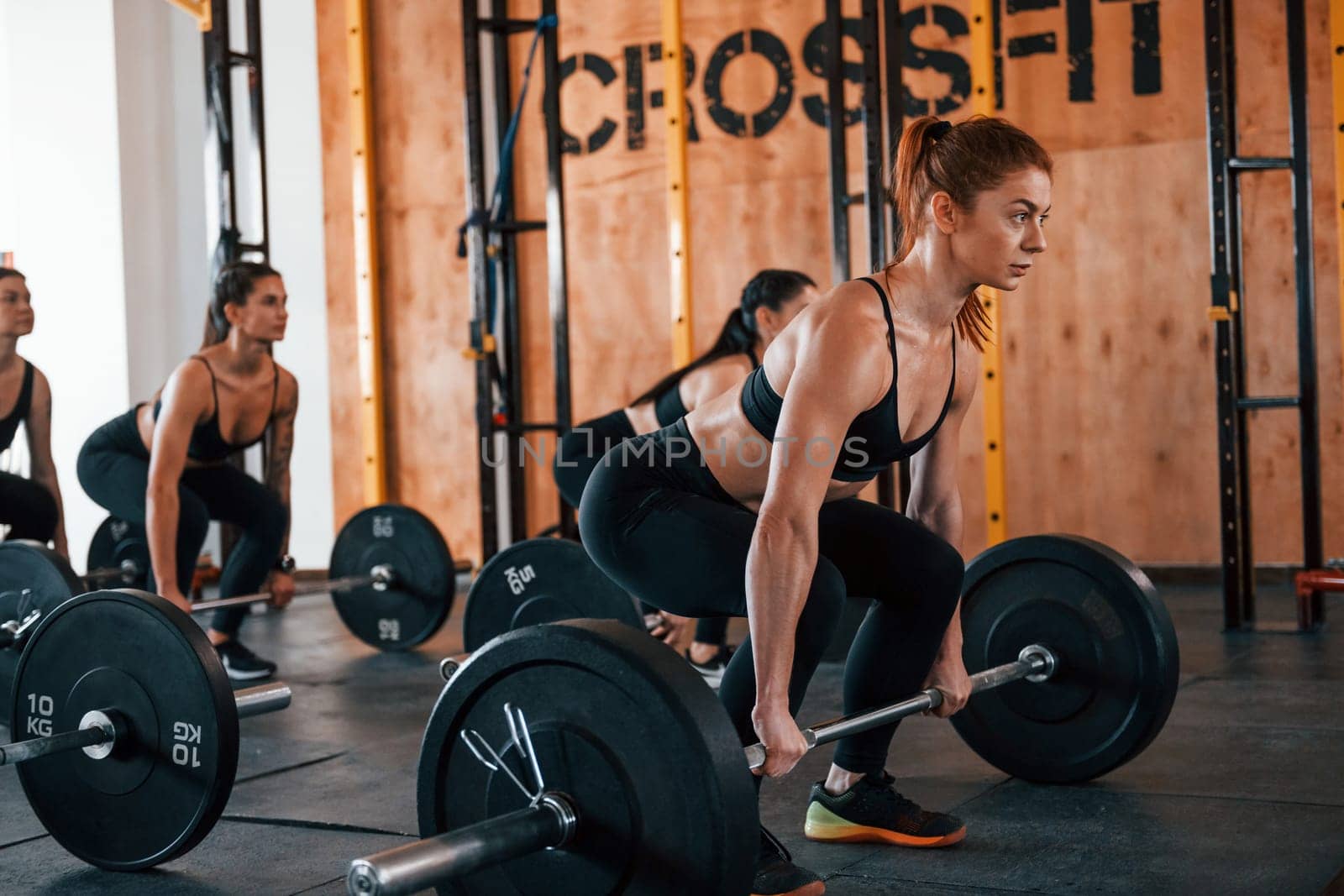 Together with barbells. Group of young sportive people have crossfit day indoors in gym.