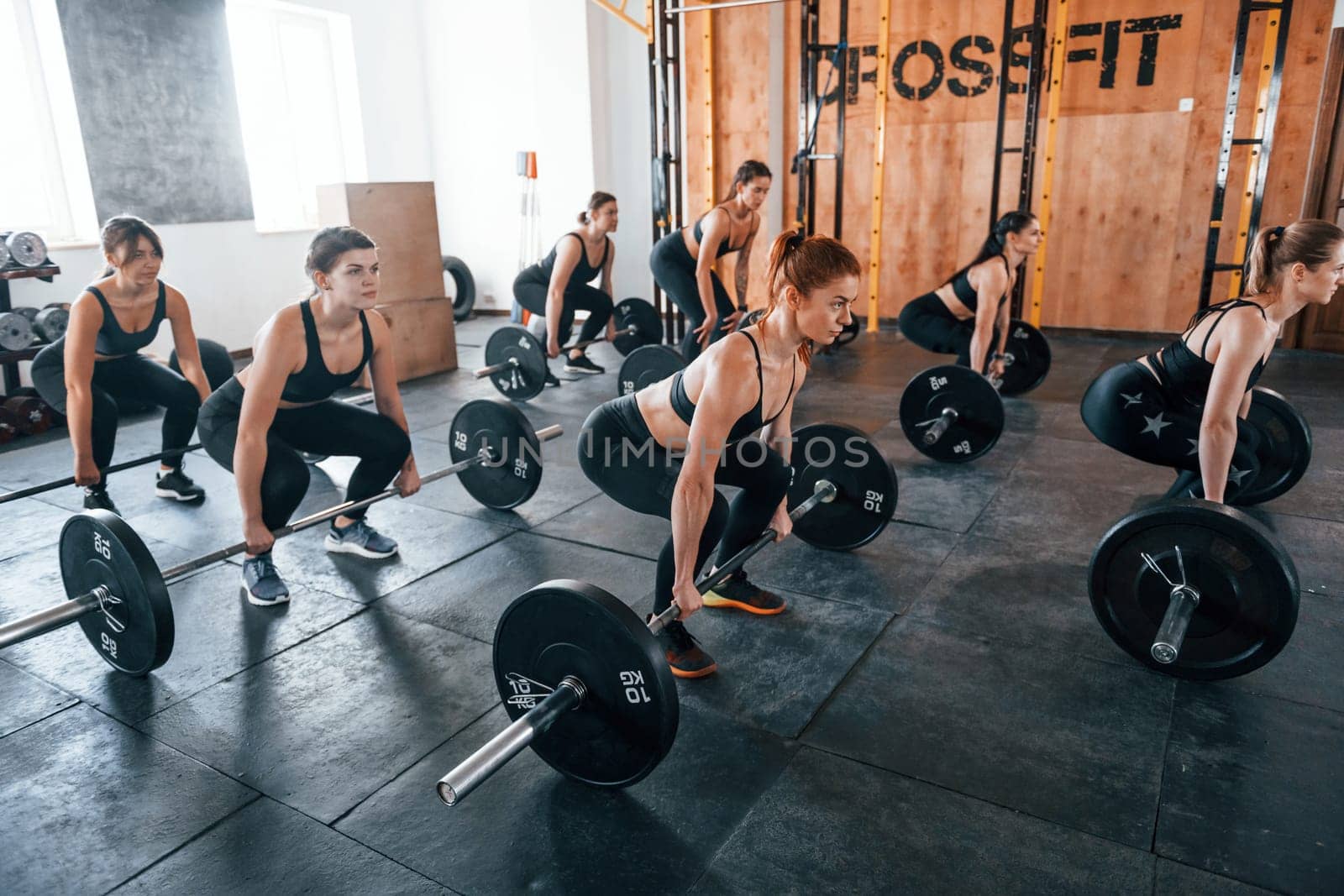 Together with barbells. Group of young sportive people have crossfit day indoors in gym.