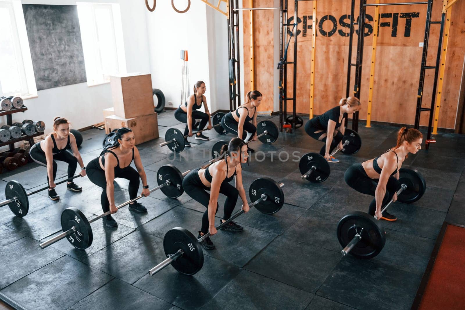 Squats with barbell. Group of young sportive people have crossfit day indoors in gym.