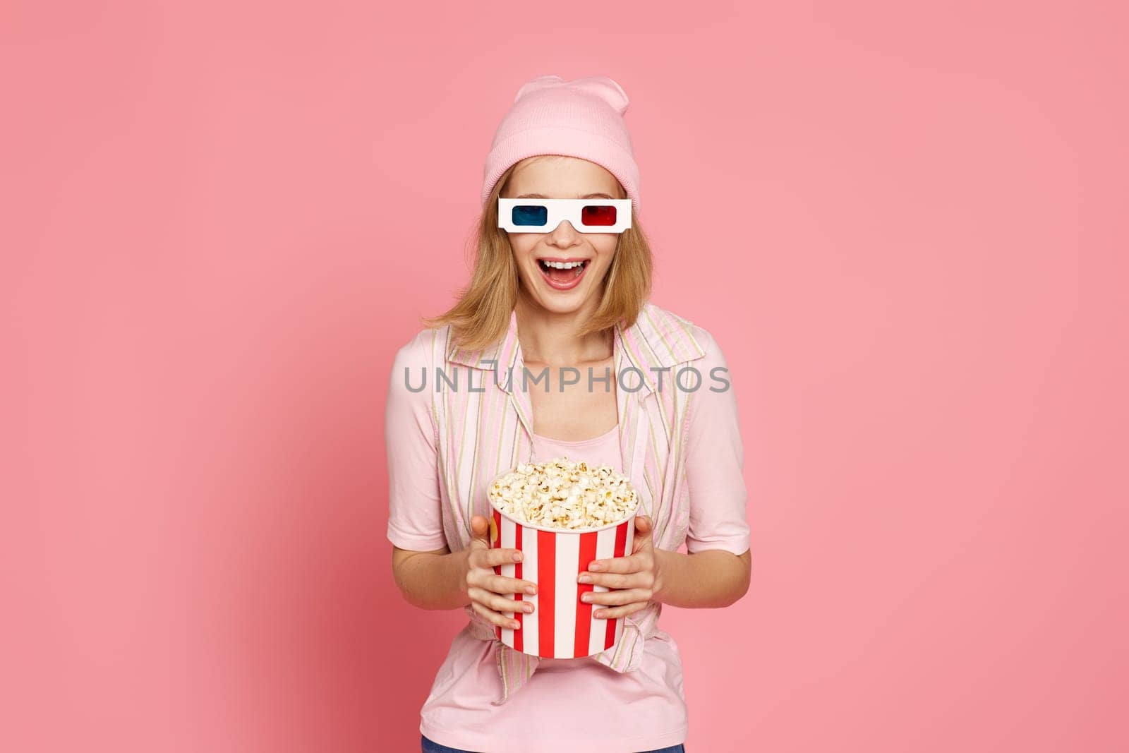 very excited young blonde woman holding bucket of popcorn on pastel pink background