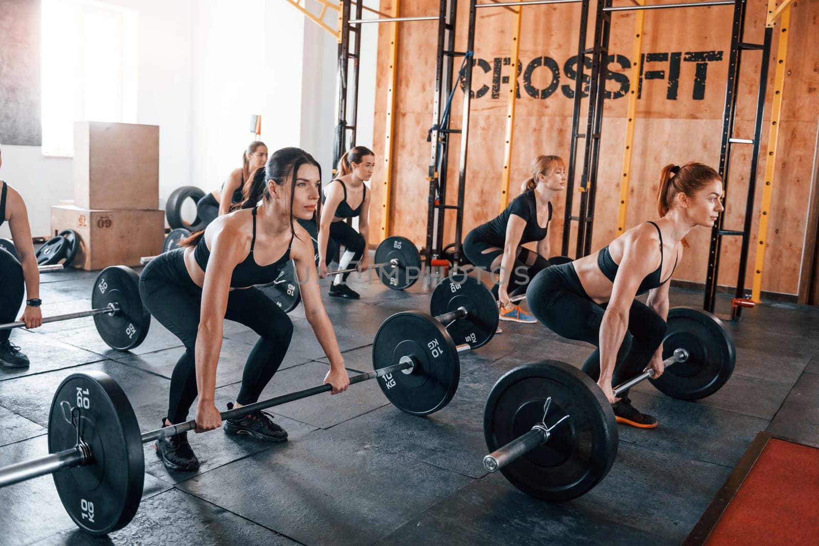 Squats with barbell. Group of young sportive people have crossfit day indoors in gym.