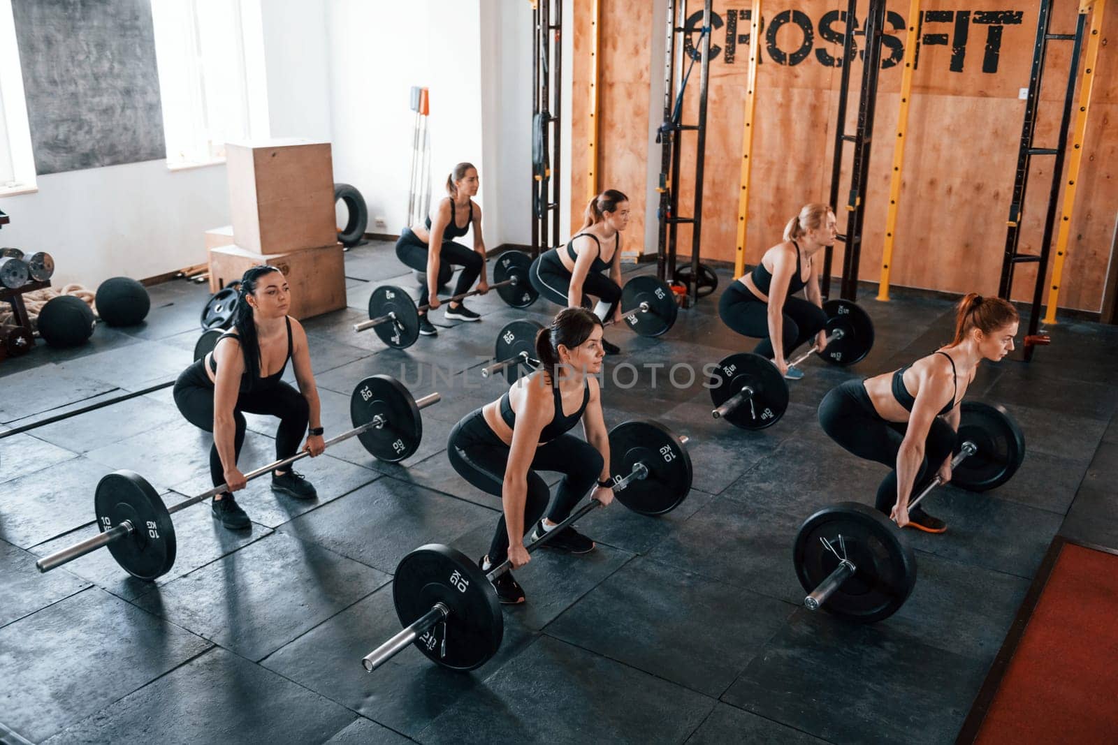 Squats with barbell. Group of young sportive people have crossfit day indoors in gym.