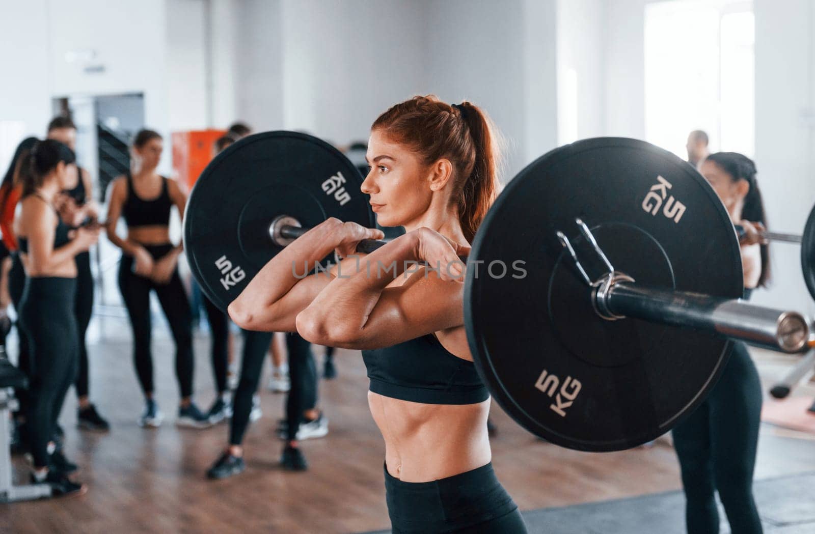 Squats with barbell. Group of young sportive people have crossfit day indoors in gym.