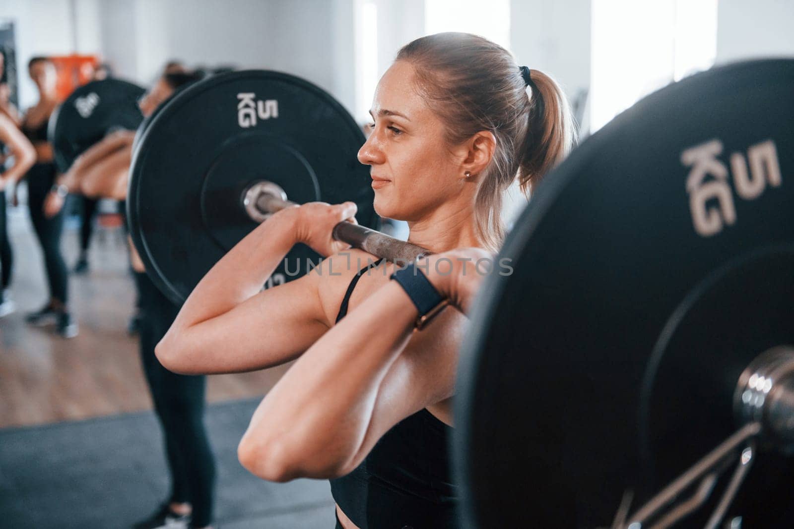 Squats with barbell. Group of young sportive people have crossfit day indoors in gym.