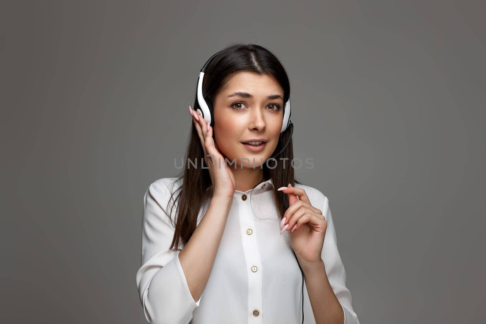 pretty helpline operator woman with headphones and microphone on gray background. girl surprised by what she heard