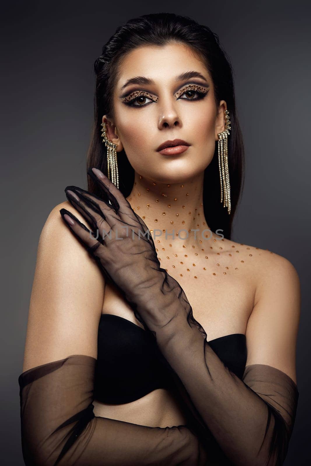 beauty fashionable model woman with creative eye makeup with arrows and rhinestones in long earring on gray background