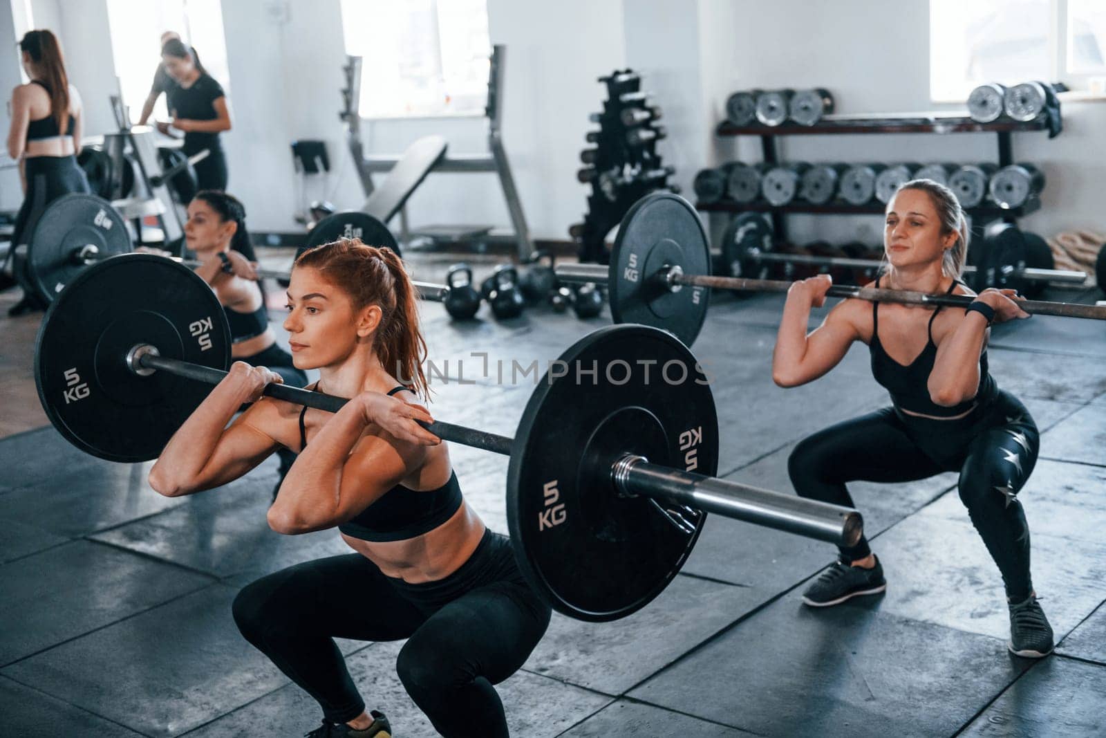 Squats with barbell. Group of young sportive people have crossfit day indoors in gym.