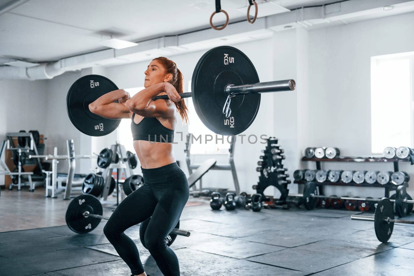 Young fitness woman with slim type of body doing exercises by using barbell.