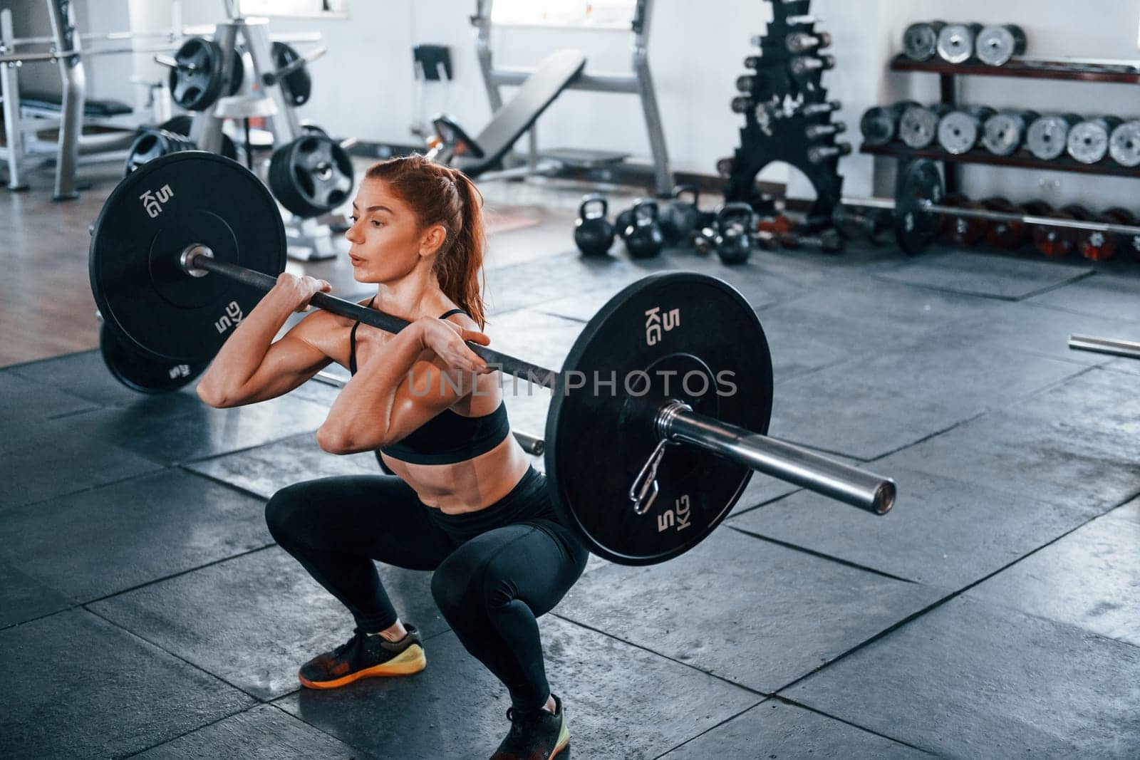 Young fitness woman with slim type of body doing exercises by using barbell.