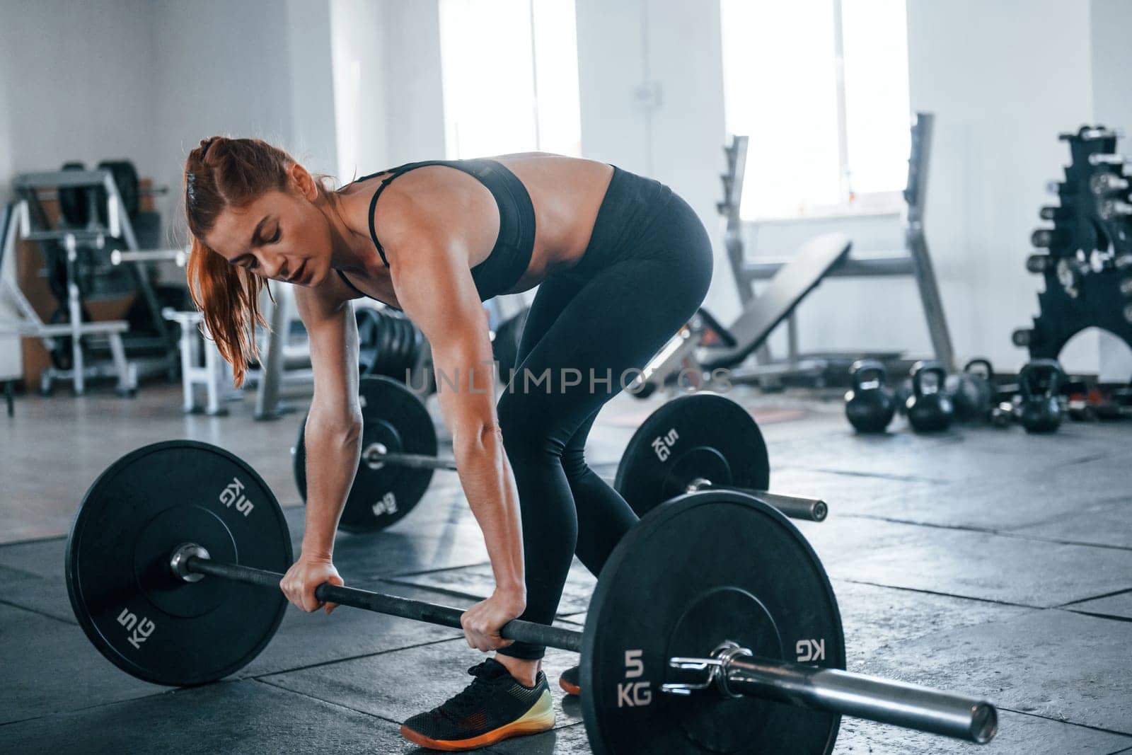 Young fitness woman with slim type of body doing exercises by using barbell.