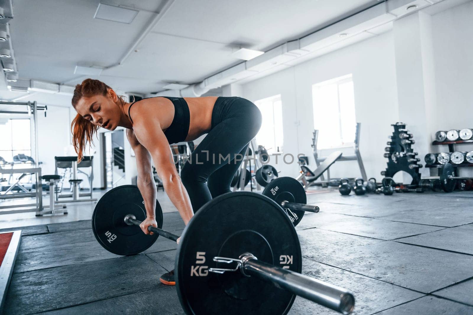 Young fitness woman with slim type of body doing exercises by using barbell.