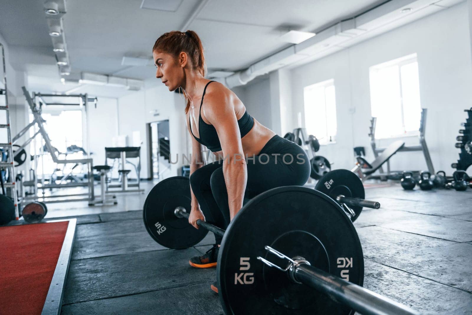 Young fitness woman with slim type of body doing exercises by using barbell.