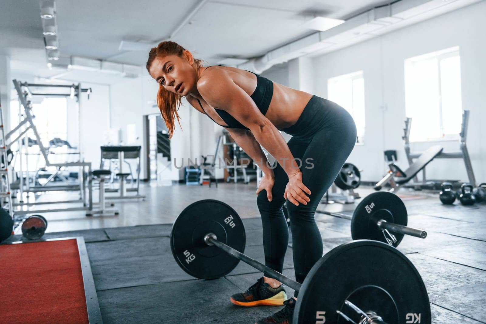 Young fitness woman with slim type of body doing exercises by using barbell.