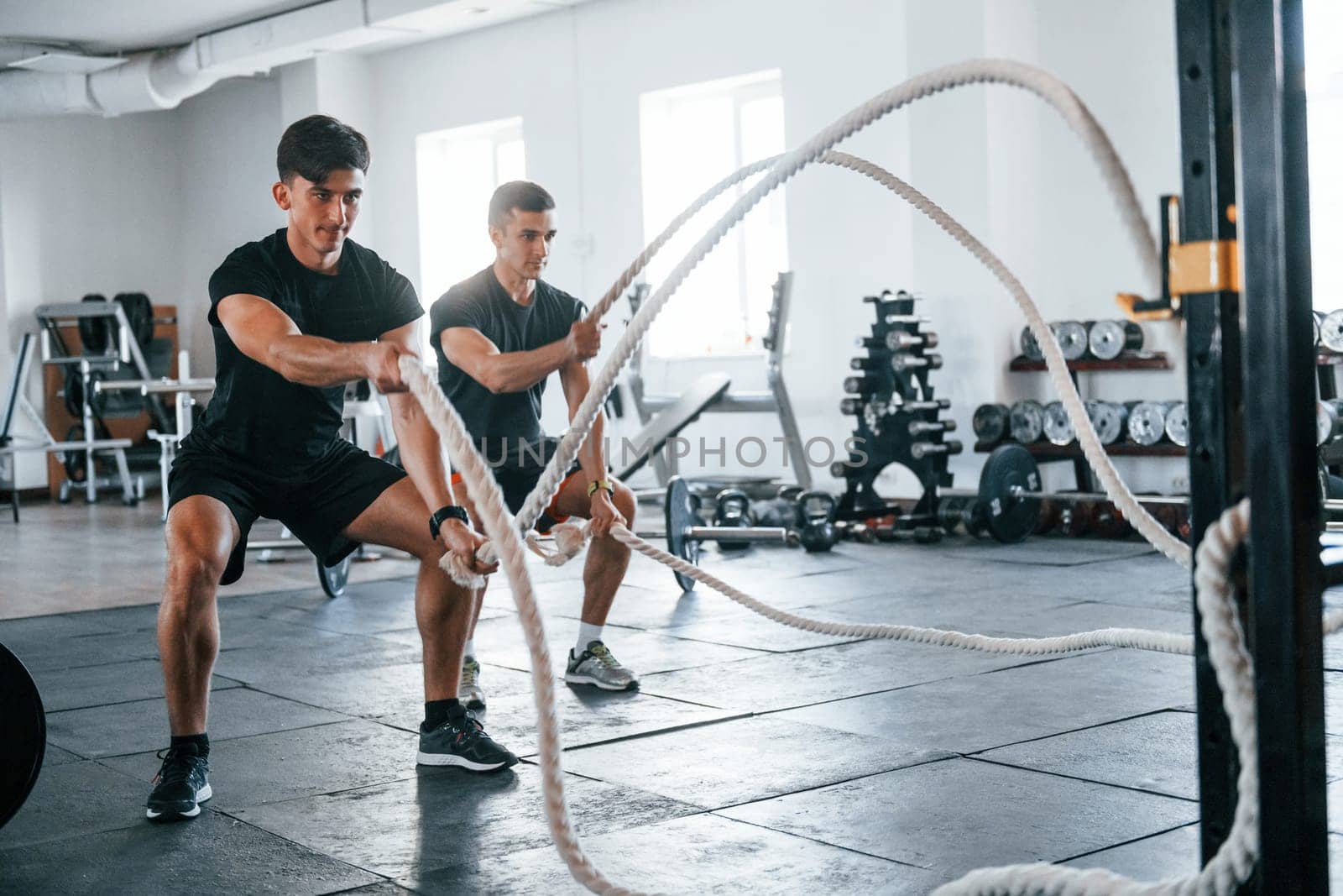 Young people with sportive body shapes doing crossfit by using knots.