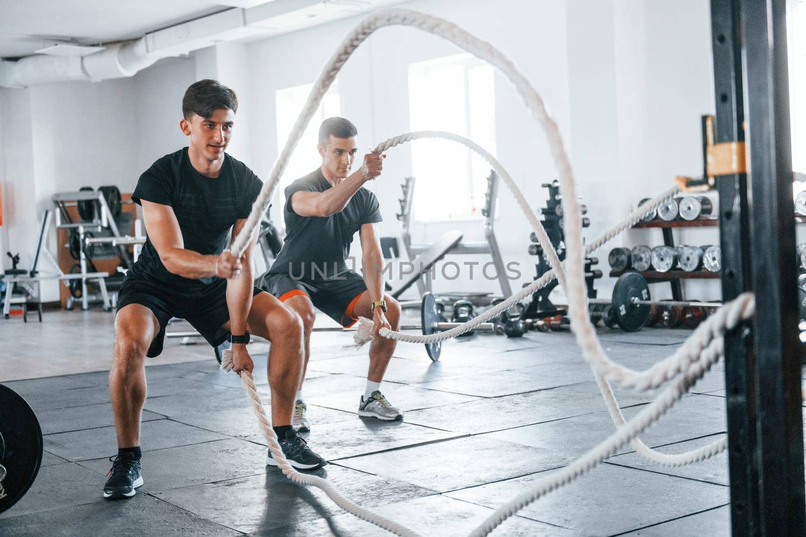 Young people with sportive body shapes doing crossfit by using knots.